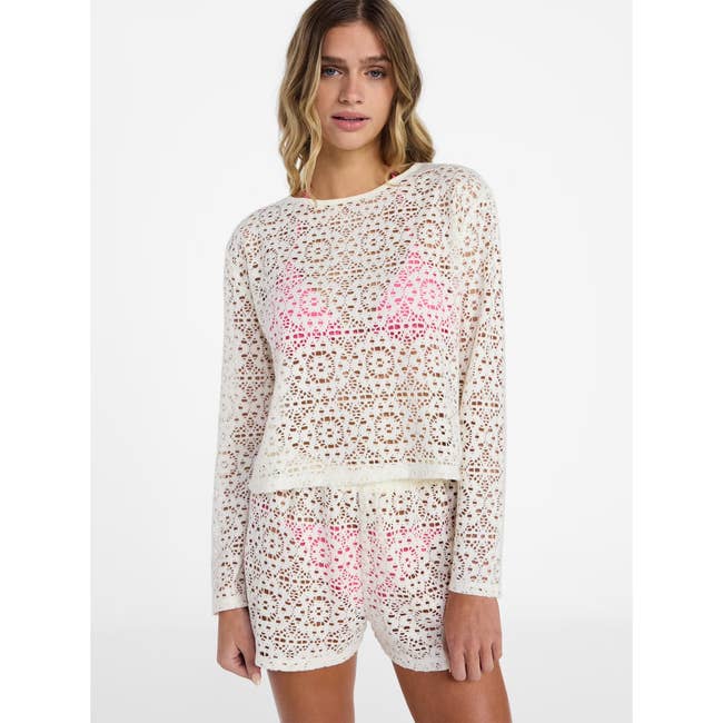 Person wearing a crochet-style knit top and matching shorts with a pink swimsuit underneath