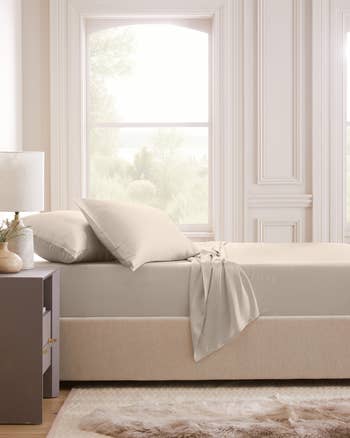 Minimalist bedroom featuring a neatly made bed with soft sheets, a furry rug, and large windows with natural light filtering in