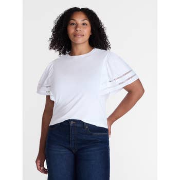 Person wearing a white top with ruffled sleeves and jeans, standing confidently