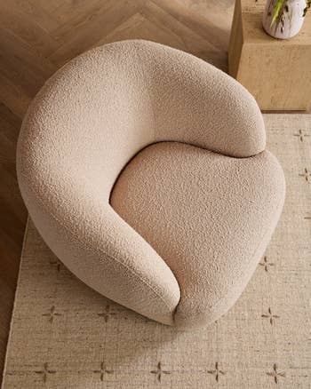 Curved, textured armchair placed on a patterned rug, with a minimalist wooden table beside it