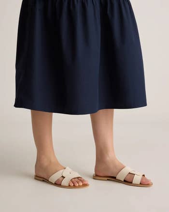 Person wearing a knee-length skirt and stylish slip-on sandals, showcasing a casual, trendy shopping look