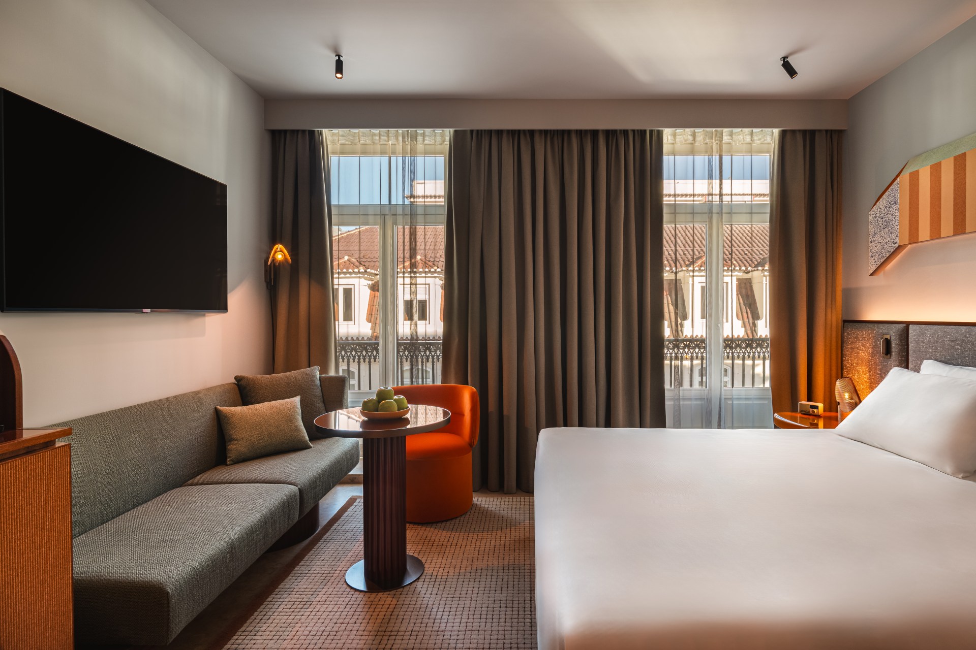 The standard king bedroom at the Andaz Lisbon. There are floor-to-ceiling windows, a bed, a sofa and a TV mounted on the wall.