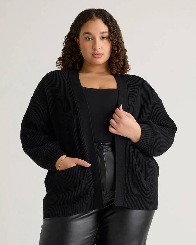 Person wearing a stylish oversized cardigan over a black top and leather pants, posing confidently