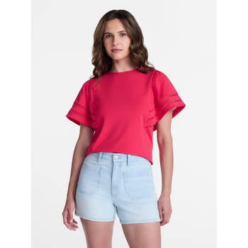 Person wearing a short-sleeve top with lace details and light denim shorts