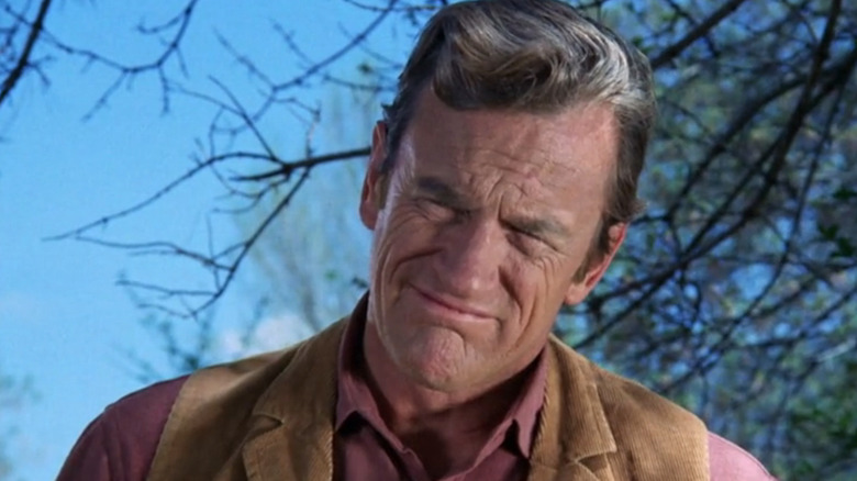 James Arness' Matt Dillon looks down and squints as he stands against a blue sky in Gunsmoke
