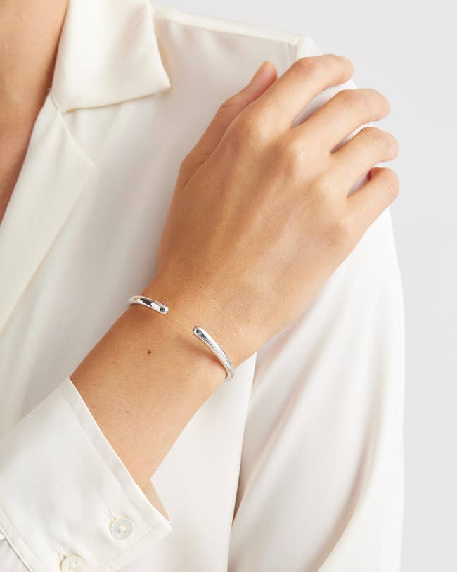 Person wearing a minimalistic open bangle bracelet on their wrist, styled with a classic collared shirt