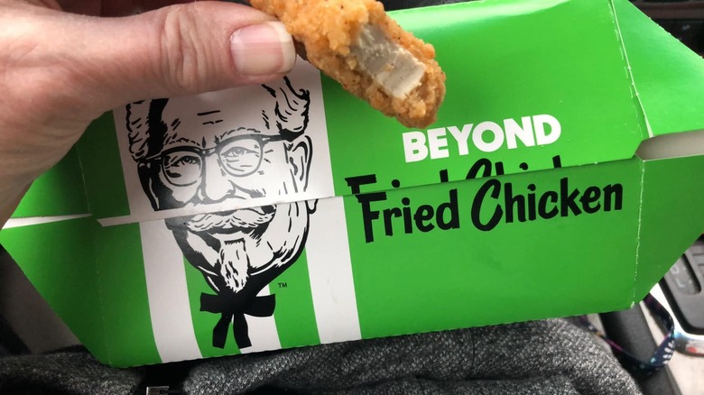 KFC Beyond fried chicken box with hand holding partially-eaten Beyond fried chicken nugget