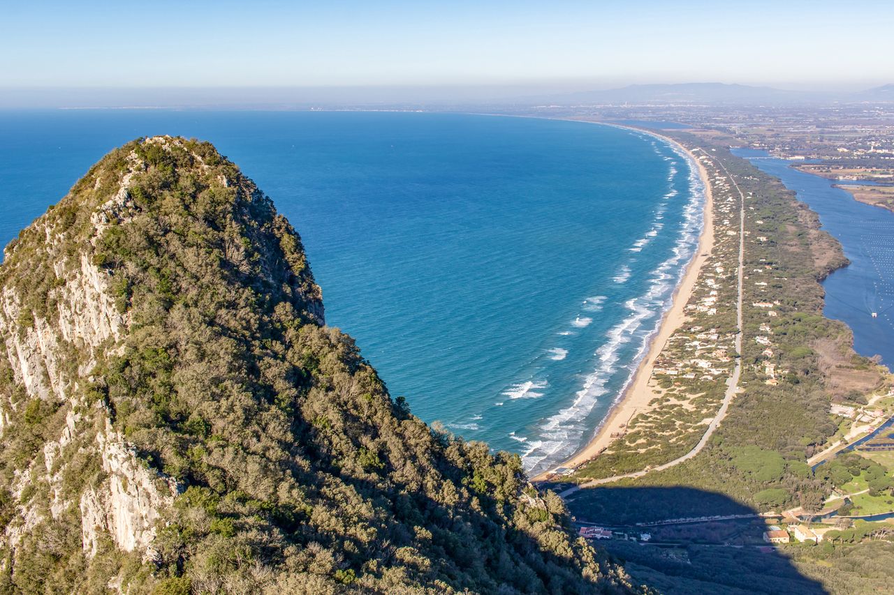 Aerial view of a coastal landscape with a mountain and a long stretch of beach adjacent to the sea