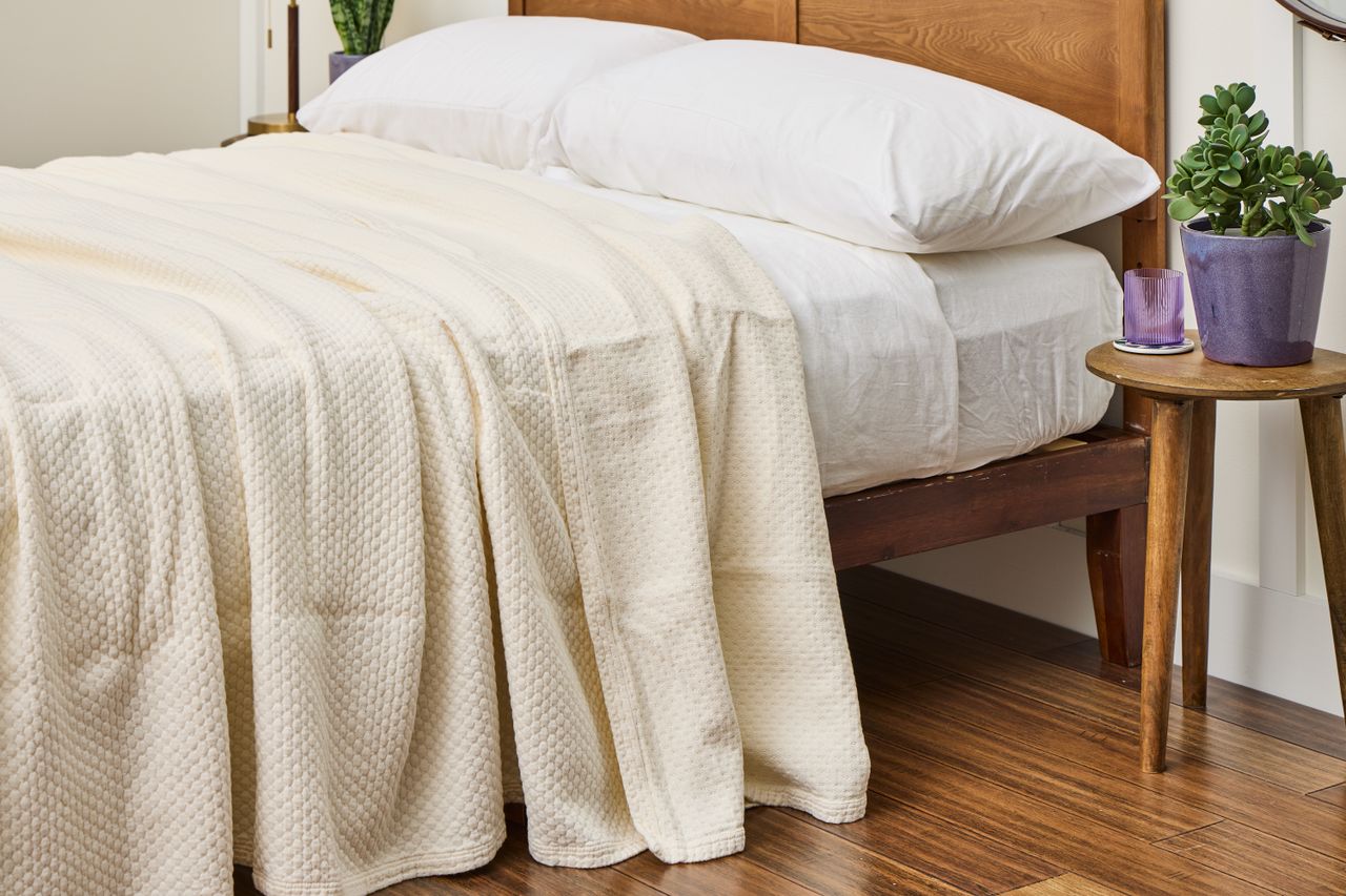 A textured bedspread draped on a neatly made wooden bed with two white pillows