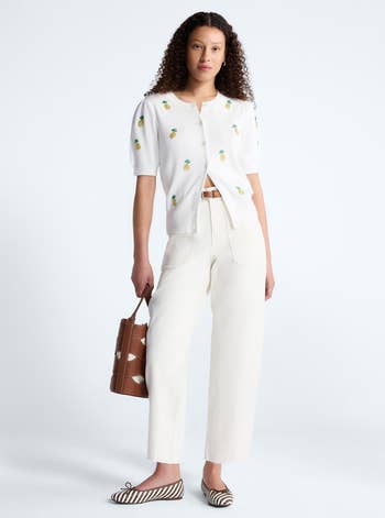 Person wearing a short-sleeve top with embroidered details, wide-leg white jeans, and holding a stylish handbag