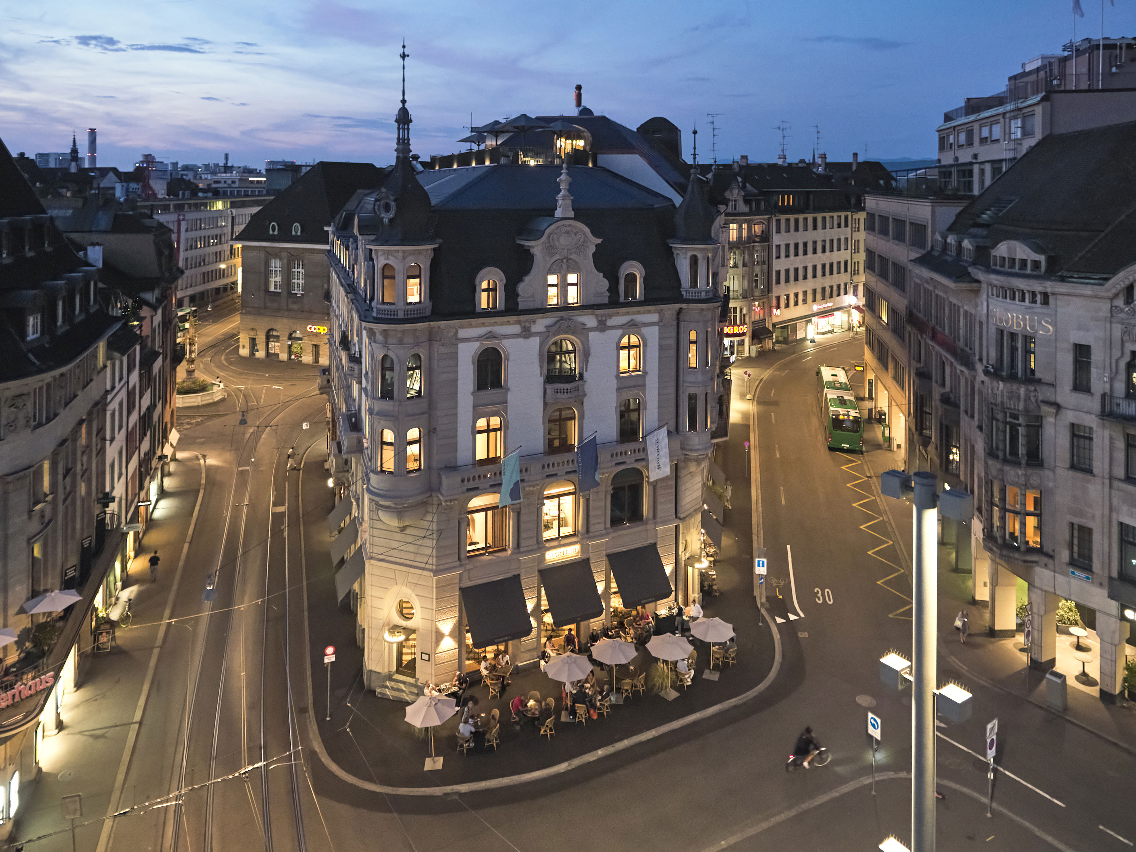 Photos of the exterior of Hotel Märthof Basel, based in a beautiful square with historical landmarks with umbrella-covered tables dining at the bar outside