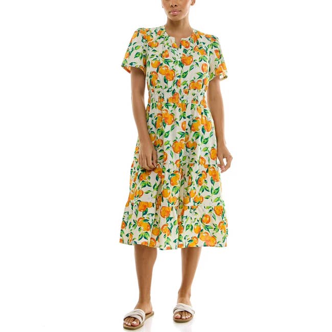Person wearing a knee-length dress with a citrus fruit pattern and sandals, suitable for a casual summer outing