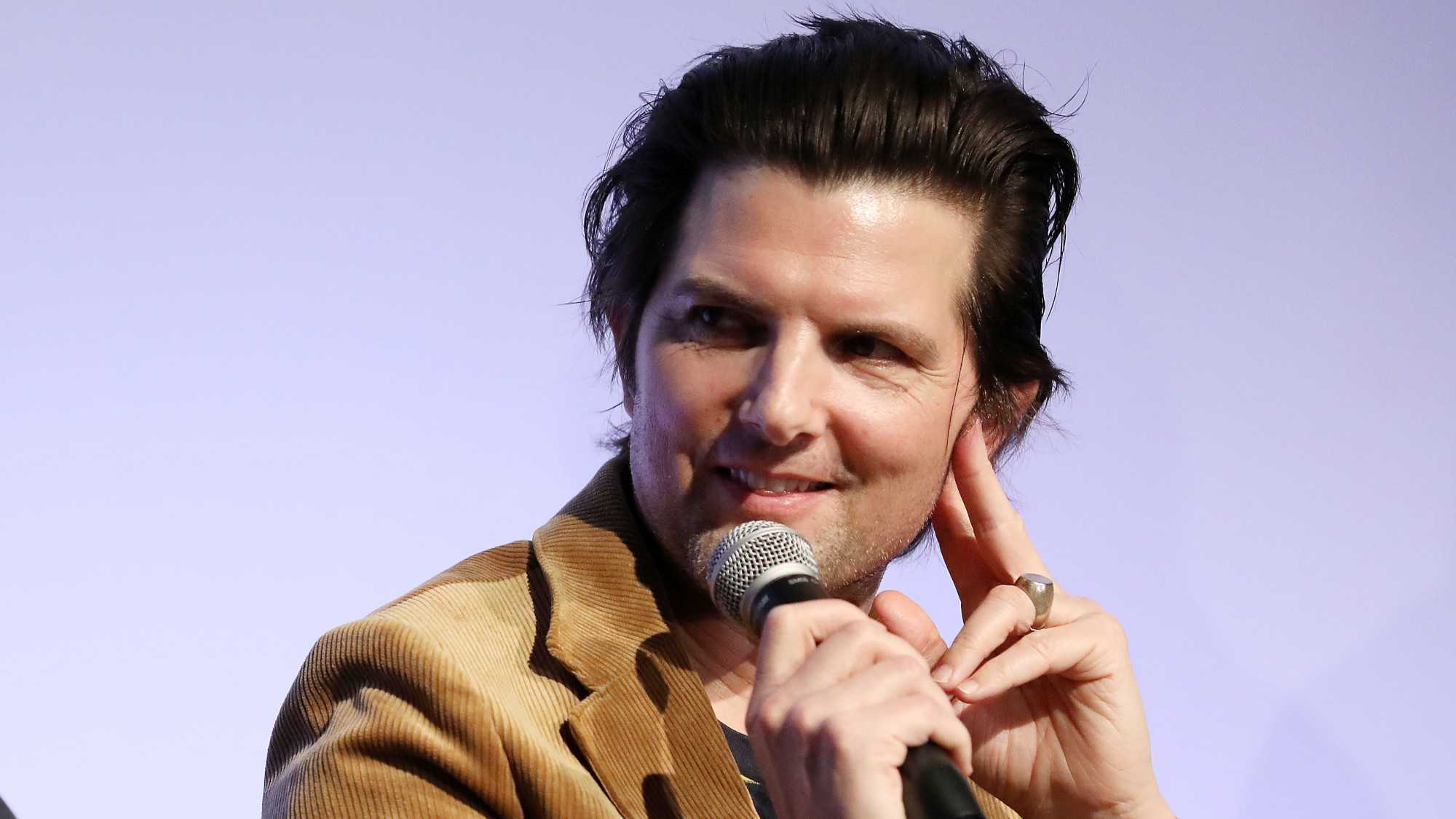 Adam Scott smiles while listening to a speaker at a Q&A event