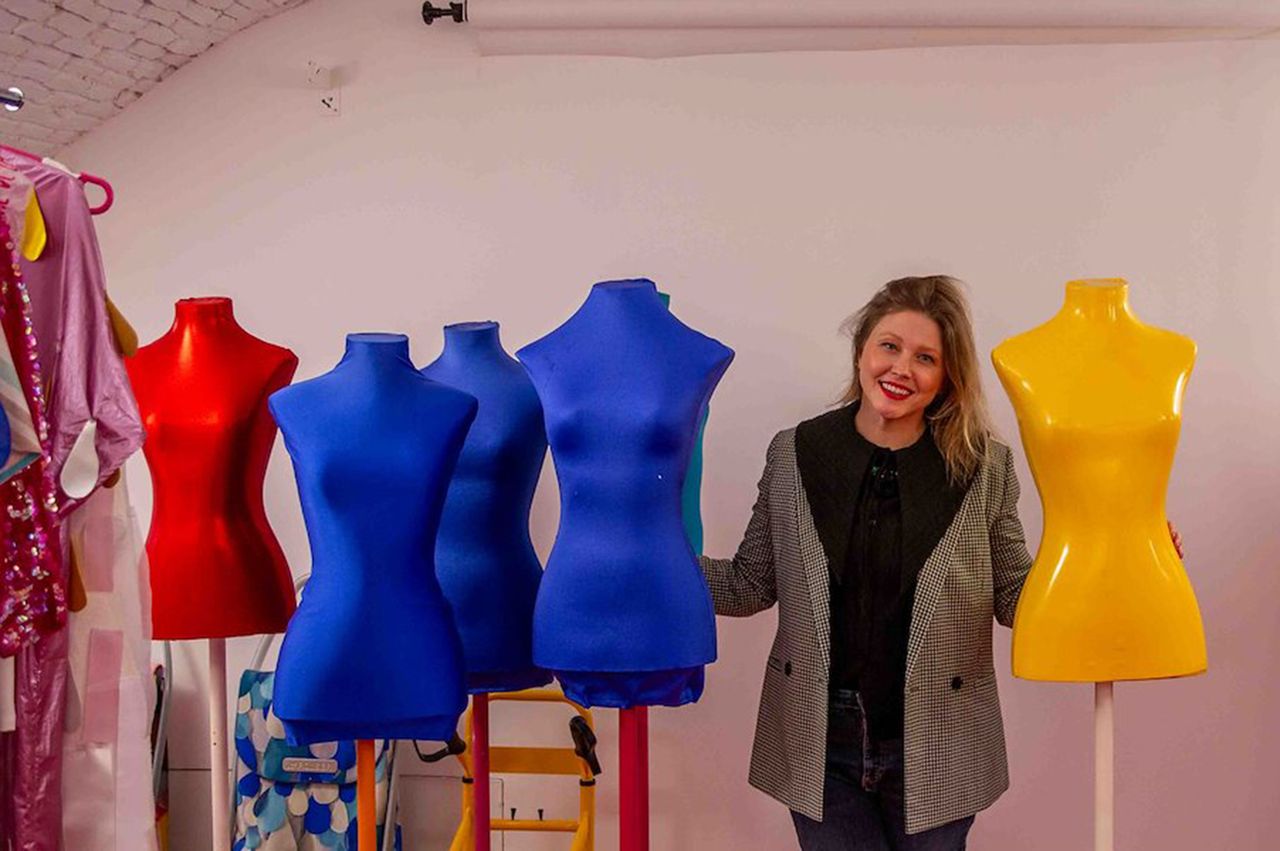 A person stands smiling next to a group of colorful mannequins in a studio