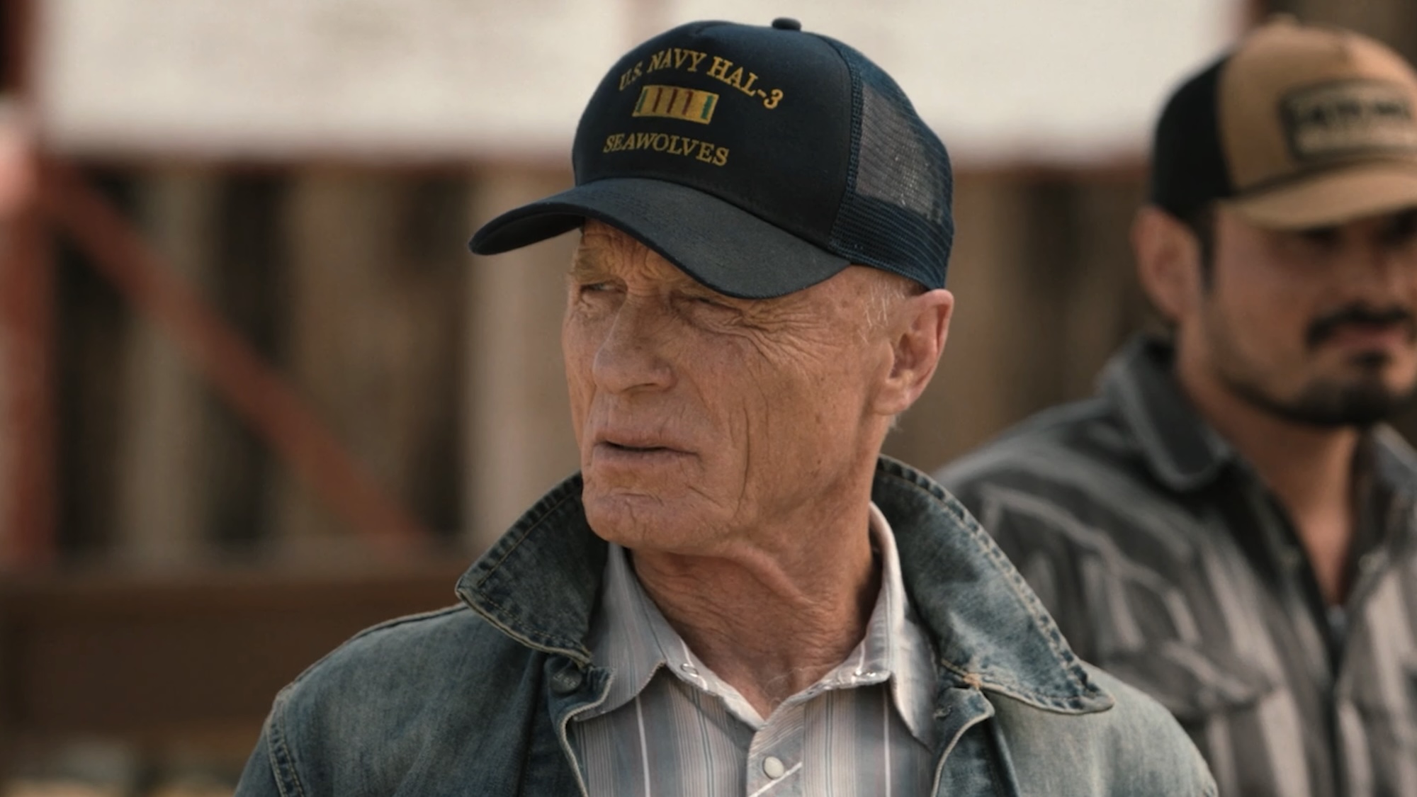 Everett in trucker cap and denim jacket talking to Beth about cattle scars in Dutton Ranch