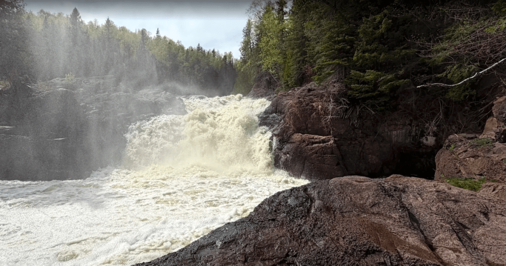 Rushing whitewater of Upper Falls on the Brule River surrounded by mist and pine trees in Minnesota.