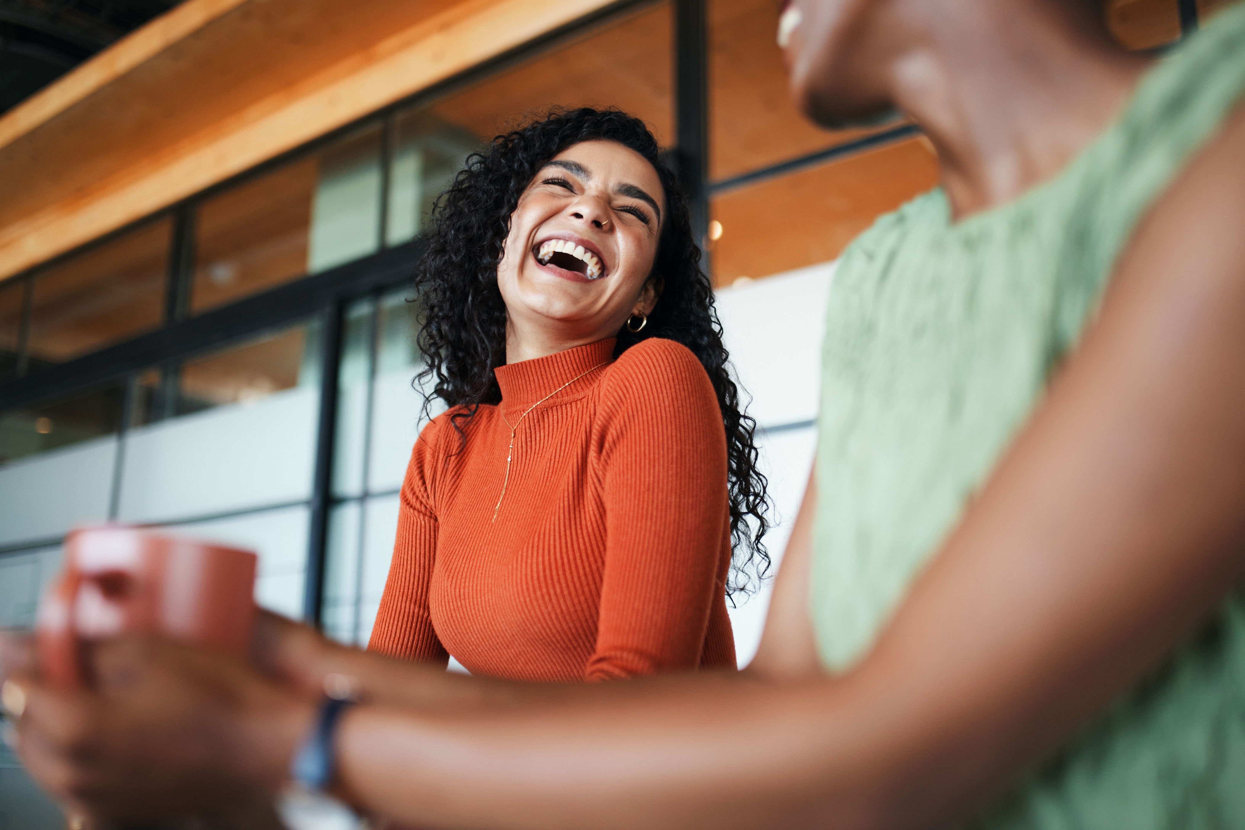 Two people laughing and enjoying coffee, one wearing a stylish long-sleeve shirt, creating a warm and joyful atmosphere