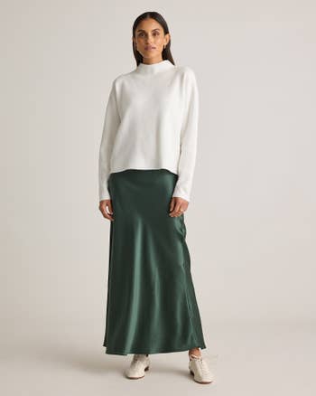 Person wearing a white sweater and a long, flowing dark skirt with white sneakers