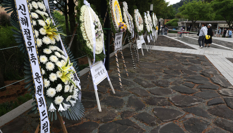 White floral wreaths with condolence ribbons line a stone path at Bongha Village during a memorial event.