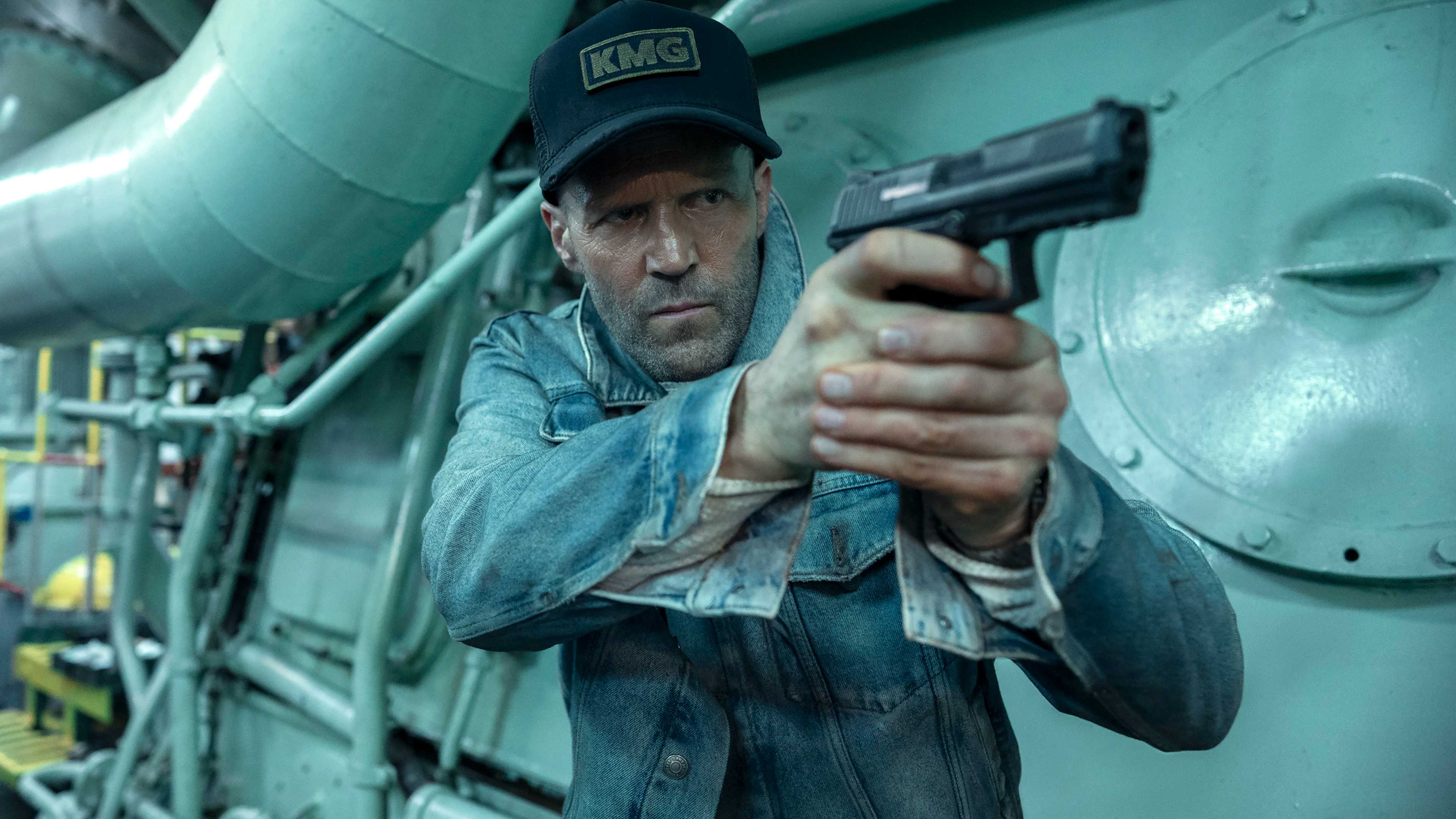 Jason Statham's Cole looking intense and aiming a gun while in an engine room in Mutiny