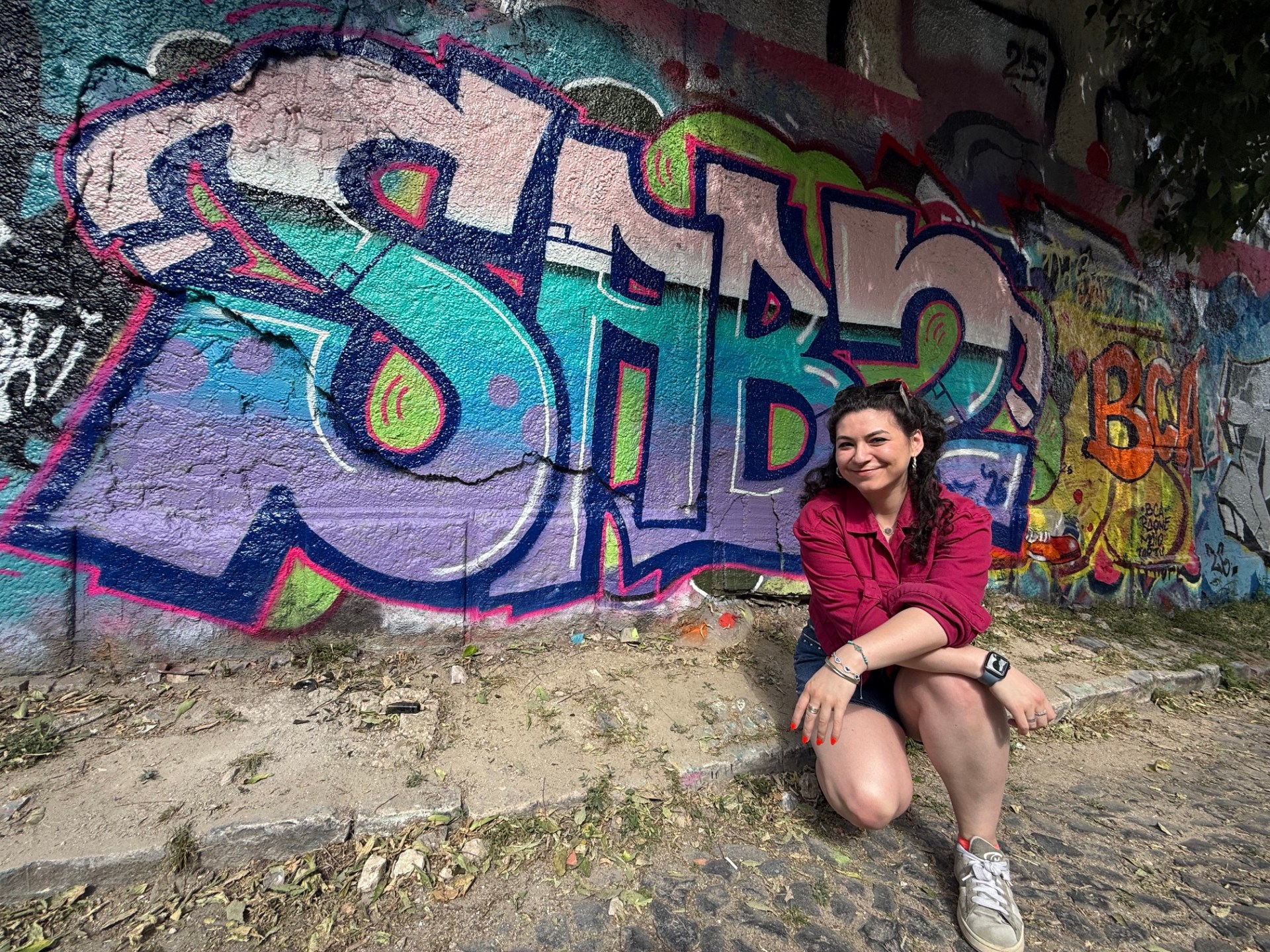 Sabrina Barr crouching in front of the 'Sabz' tag she graffitied in Lisbon on a street art tour.