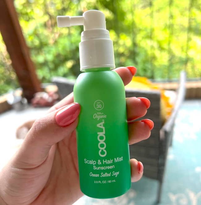Hand holds a green bottle of Coola Scalp & Hair Mist with SPF 30, labeled