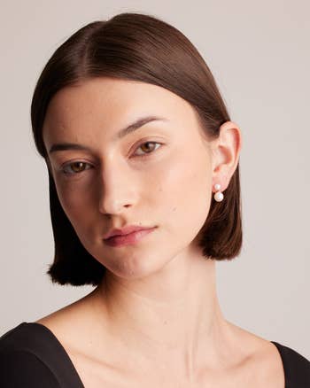 Person wearing simple pearl earrings, with short straight hair, looking directly ahead with a neutral expression