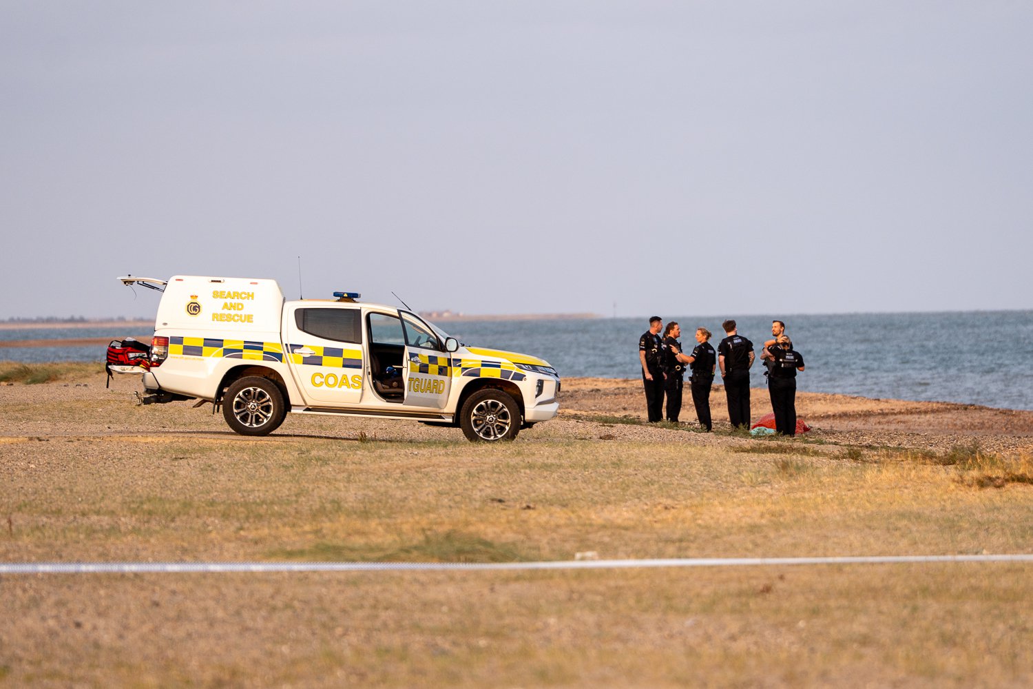 Police standing on beach with truck behind htem