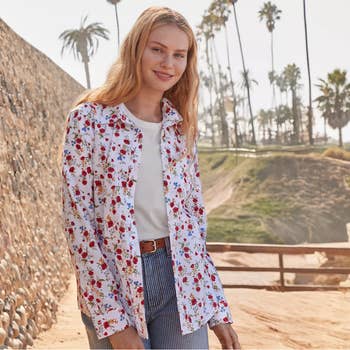 Person wearing a floral button-up shirt and jeans, standing outdoors with palm trees in the background