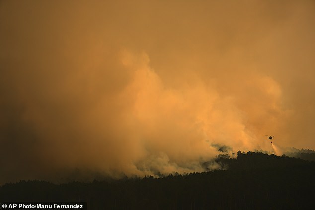 A firefighting helicopter drops water on the flames as a wildfire advances near Condemios de Arriba, Guadalajara province, Spain, Wednesday, July 22