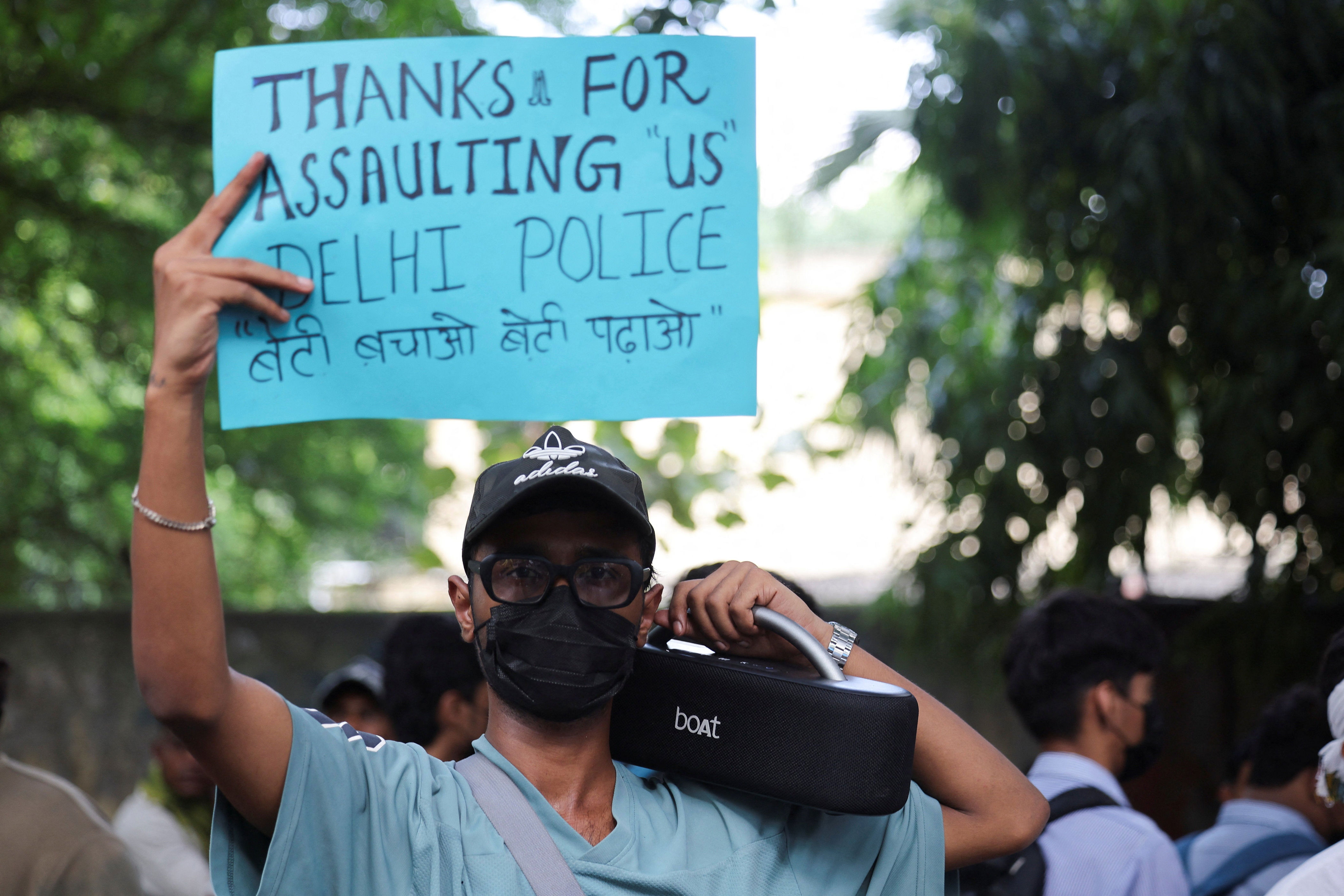 A protester hold placard mocking Delhi Police for assaulting the youth on ground demanding resignation of education minister Dharmendra Pradhan (Reuters)