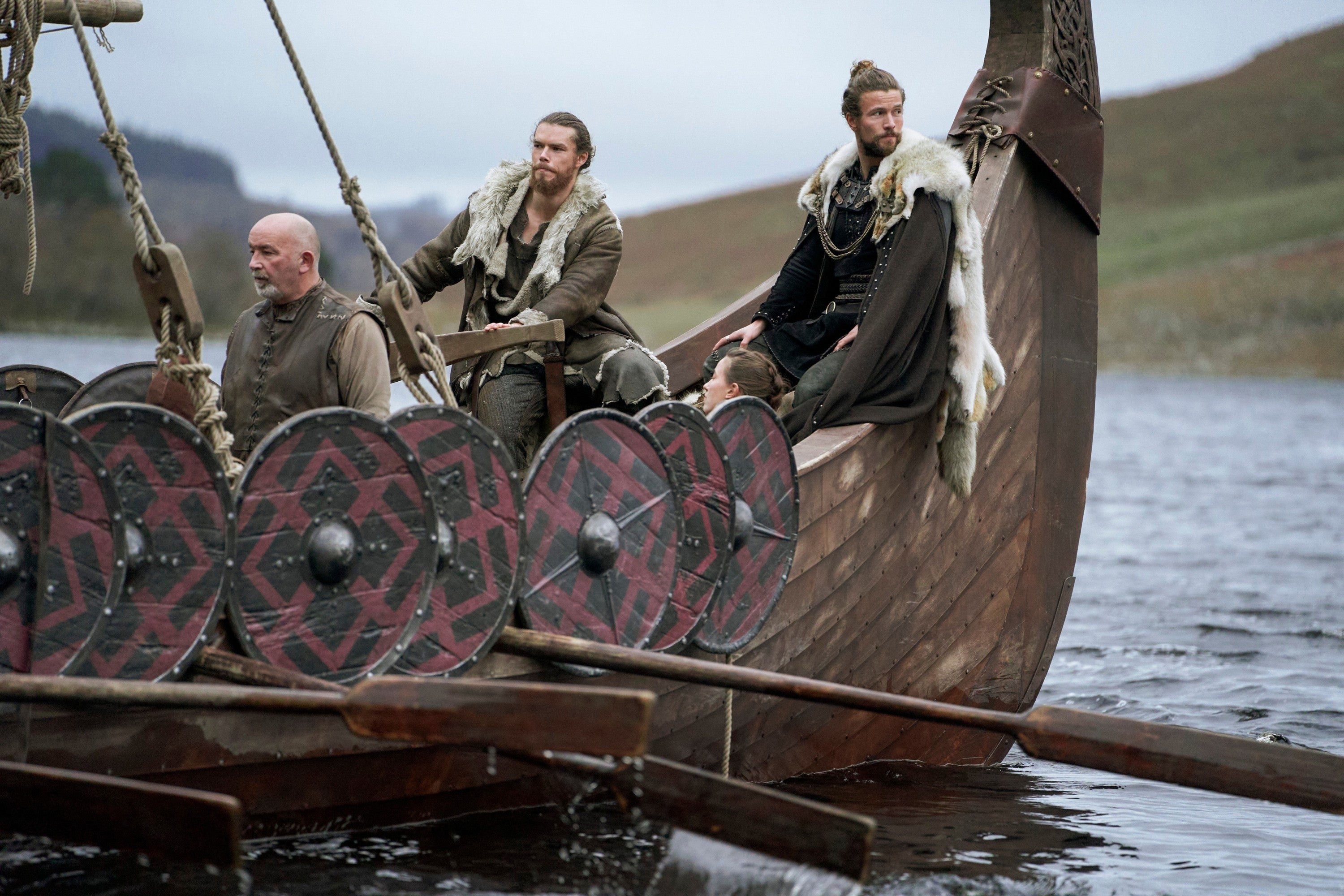 People in Viking-style costumes on a wooden boat with shields, navigating a body of water