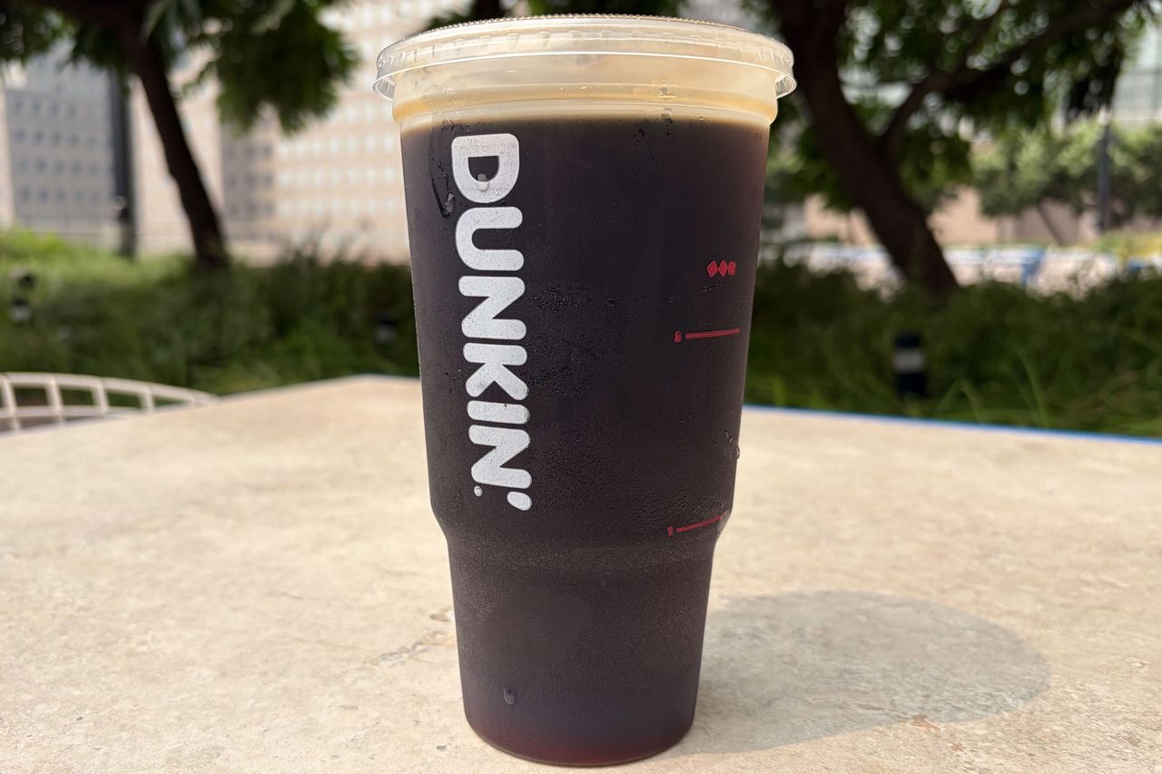 A Dunkin cold brew coffee cup outdoors on a table with blurred greenery in the background