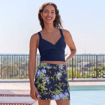Person wearing a stylish, sleeveless top and floral skirt by a poolside