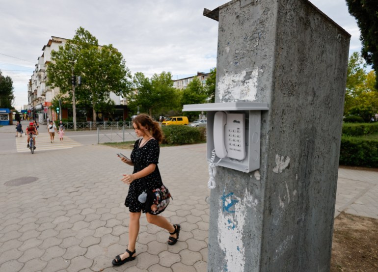 A woman uses a mobile phone as she walks past a landline public street phone for communication with emergency services when there are disruptions to the mobile network, amid the Russia-Ukraine conflict, in the Black Sea resort city of Yevpatoriya, Crimea, July 21, 2026. REUTERS/Alexey Pavlishak