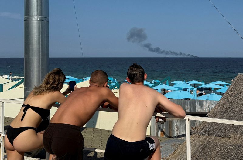 People look at a ship burning at sea in Odesa
