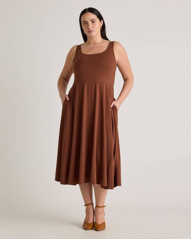 Person wearing a sleeveless, knee-length dress with a scoop neckline, featuring a flowy skirt and pockets