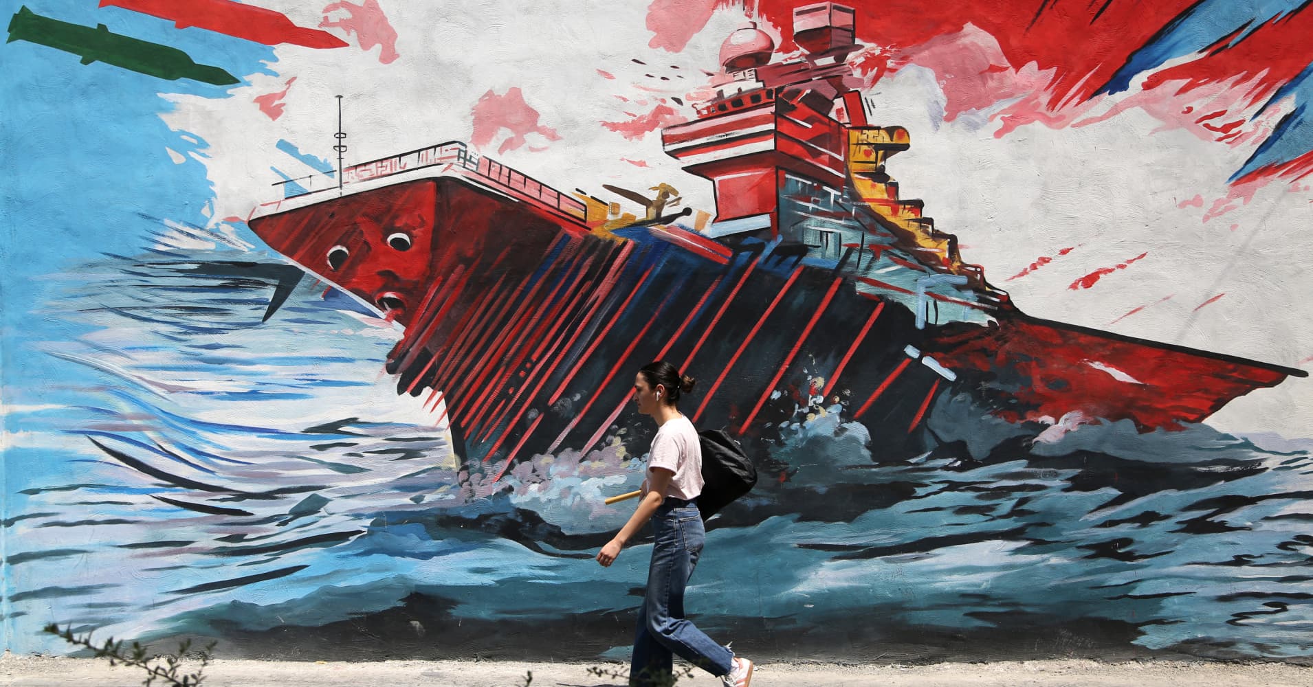 A woman walks past war-themed graffiti and murals painted on walls along the capital Tehran's streets and avenues as air defense systems are activated during the night while daily life continues in the shadow of rising military tensions between the US and Iran on July 22, 2026 in Tehran, Iran.