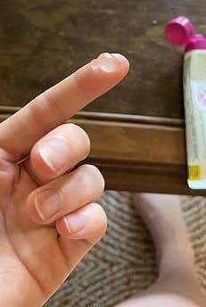 Finger with a small dab of translucent gel, suggesting skincare or cosmetic product use next to an open bottle on a table