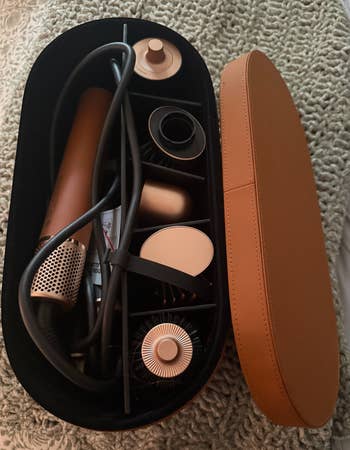 Hair styling tool set with various attachments neatly arranged in an open, oval-shaped travel case on a textured surface