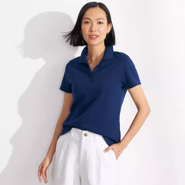 Person wearing a collared short-sleeve shirt and white pants poses against a plain background