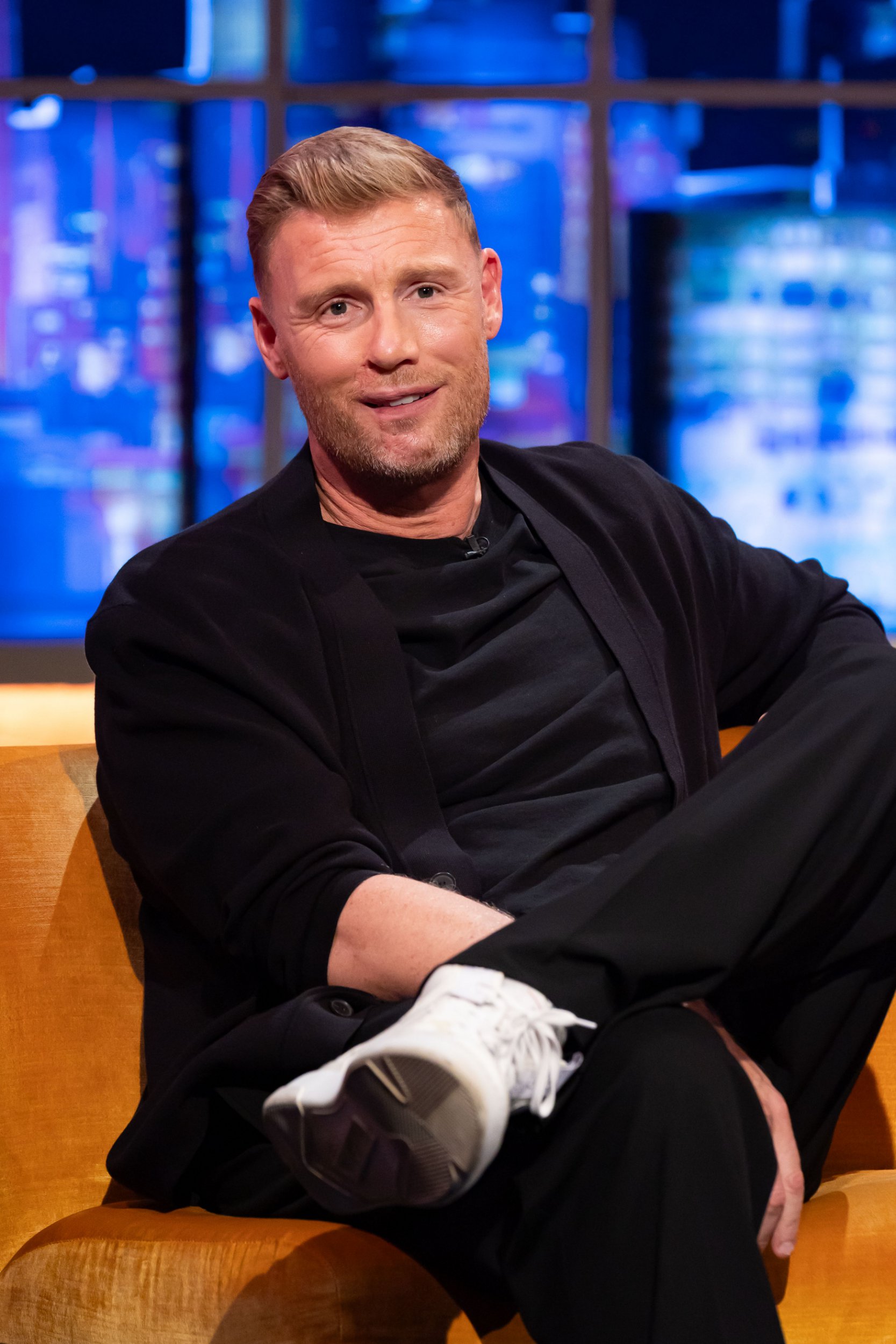 Freddie Flintoff sits on orange chair, wearing black suit