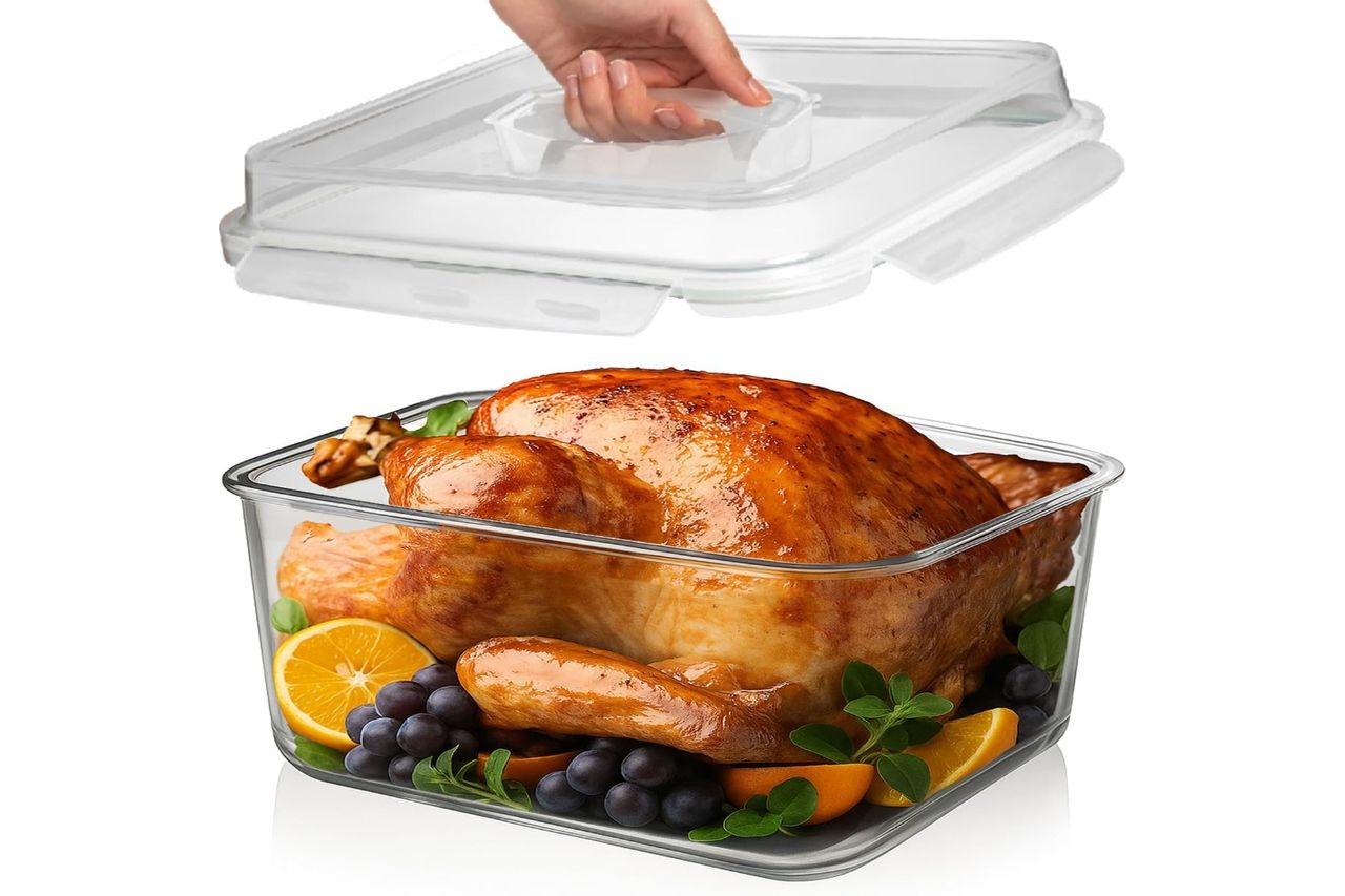 Glass food storage container holding a cooked turkey with fruits and a hand placing the airtight cover on top
