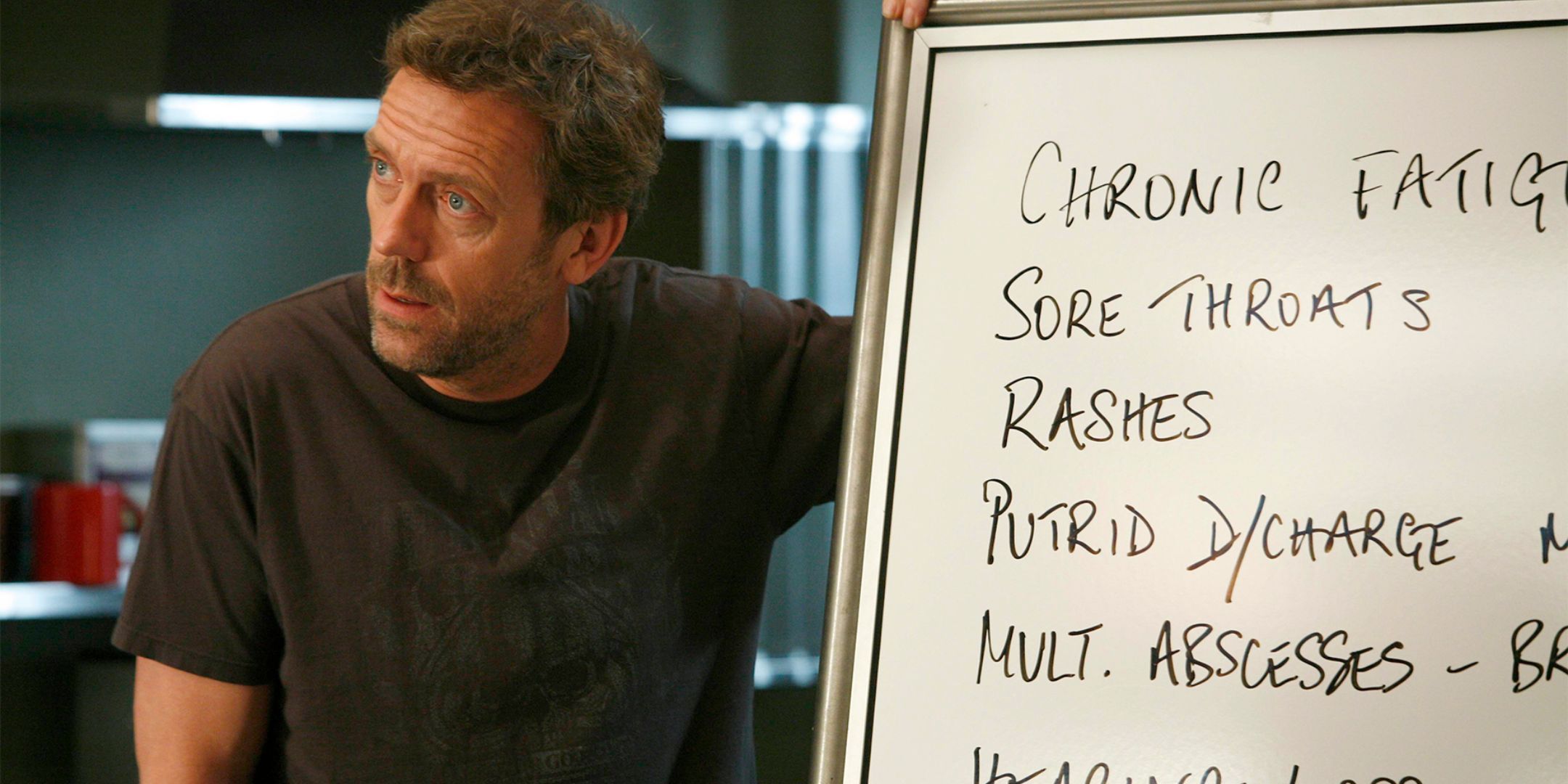 Hugh Laurie as House MD stands next to a whiteboard with a list of symptoms.