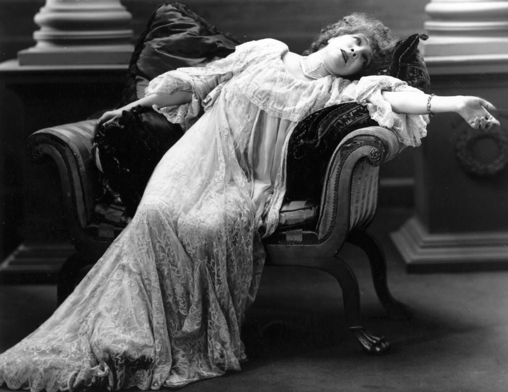 Vintage photo of a woman in an elaborate lace gown, reclining dramatically on an ornate chaise longue