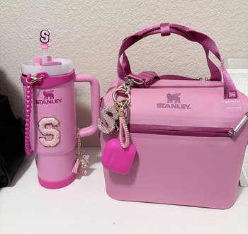 Stanley brand pink tumbler and lunchbox with keychains, featuring glittery letter