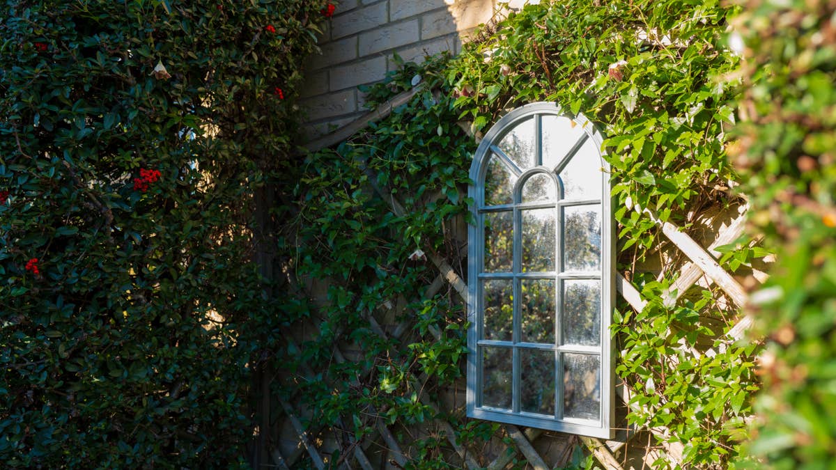 ornate-garden-mirror-giving-the-illusion-of-a-arched-window-seen-against-strong-winter-sun