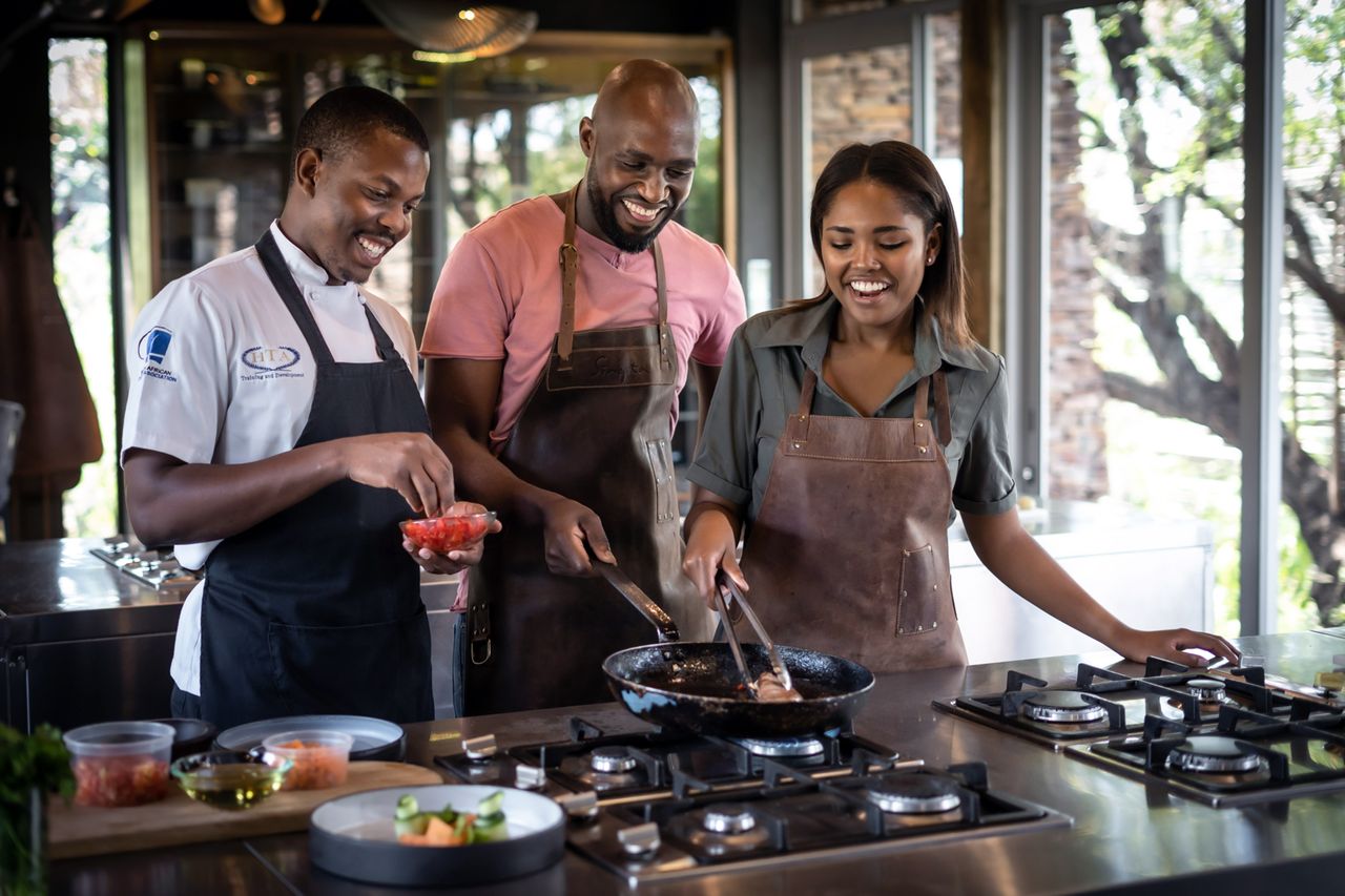 Three people cooking together in a professional kitchen setting