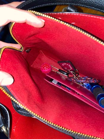 Open handbag showing keys, a pen, and other small personal items inside a red-lined interior