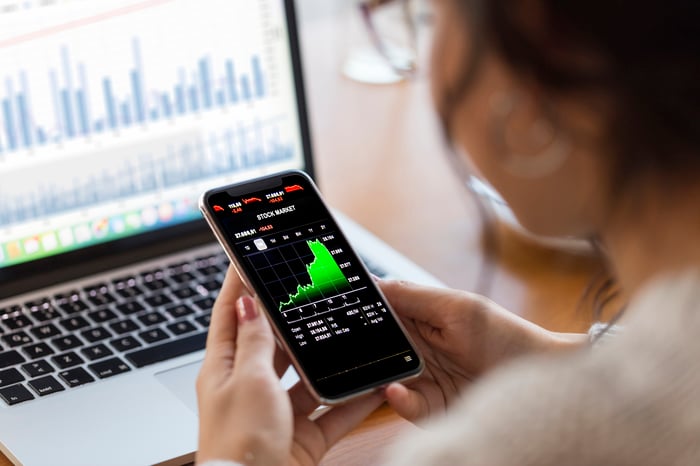 A retail investor holding a smartphone that's displaying a rapidly rising stock chart.